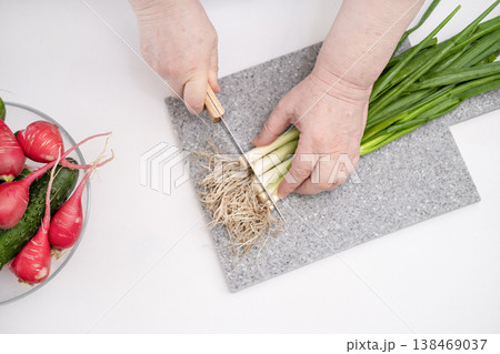 Female hands cutting green onions on a grey board Female hands cutting green onions on a grey board 138469037