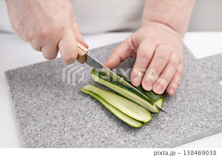 A woman's hands cutting a cucumber on a gray board A woman's hands cutting a cucumber on a gray board 138469038