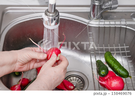 A woman's hands wash radishes under running water in the kitchen A woman's hands wash radishes under running water in the kitchen 138469076