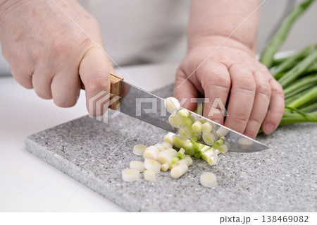 Female hands cutting green onions on a grey board Female hands cutting green onions on a grey board 138469082