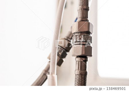 Close-up of a metal water hose connected to a water heater. The hose features a threaded connector and is made of durable material, suitable for plumbing applications. 138469501