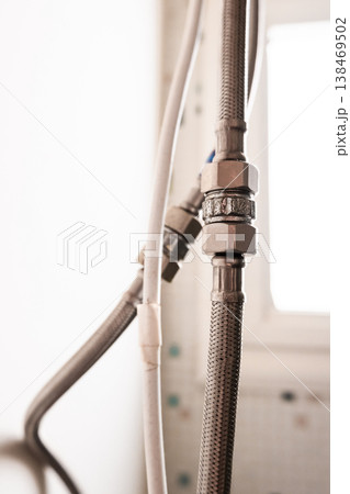 Close-up of a metal water hose connected to a water heater. The hose features a threaded connector and is made of durable material, suitable for plumbing applications. Close-up of a metal water hose connected to a water heater. The hose features a threaded connector and is made of durable material, suitable for plumbing applications. 138469502
