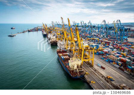 Containers are loaded and unloaded at the cargo sea port. Cranes move goods while large ships dock along the waterfront. Workers manage operations on the ships and wharf 138469686