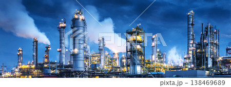 Workers operate machinery in the industrial chemical plant. The facility includes large metal towers and piping under a blue sky with clouds. The site shows activity and production 138469689