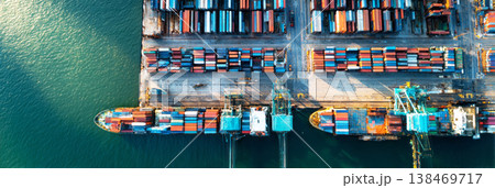 Containers are loaded and unloaded at the cargo sea port. Cranes move goods while large ships dock along the waterfront. Workers manage operations on the ships and wharf 138469717