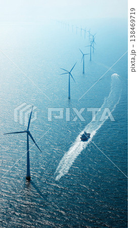 Rows of wind turbines stand tall and still in the sea, harnessing wind energy. The sun shines above and the water stretches far into the distance creating a clear view of the scene Rows of wind turbines stand tall and still in the sea, harnessing wind energy. The sun shines above and the water stretches far into the distance creating a clear view of the scene 138469719