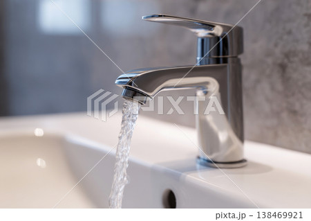 Water flows strongly from a chrome faucet into a white ceramic wash basin in a modern bathroom. The bright space highlights the cleanliness of the setting Water flows strongly from a chrome faucet into a white ceramic wash basin in a modern bathroom. The bright space highlights the cleanliness of the setting 138469921