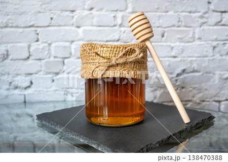 Honey glass jar with honeycomb and wood spoon stay on the stone table. Food concept. Honey glass jar with honeycomb and wood spoon stay on the stone table. Food concept. 138470388