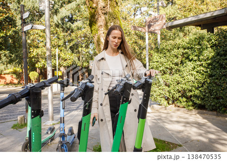 Smiling happy beautiful woman using mobile phone to unlock electric scooter in city street 138470535