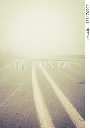 Foggy empty highway. Bad weather on the road. Road on foggy day in perspective with copy space. Driving conditions concept. Caution and danger on the road. Road marking lines on ghostly route. 138470909