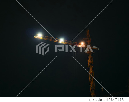 Construction crane lights up the night sky in an urban area during late hours of work Construction crane lights up the night sky in an urban area during late hours of work 138471484