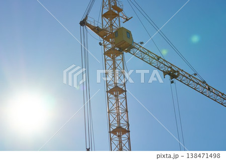 Construction crane stands tall against a clear sky during daytime work hours in an urban area with bright sunlight 138471498