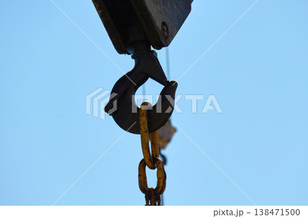 Crane hook and pulley system working at a construction site under clear blue sky Crane hook and pulley system working at a construction site under clear blue sky 138471500