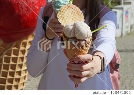 Woman holding ice cream cone with multiple scoops and waffle biscuit outdoors. Street dessert scene for summer snack, sweet food, casual lifestyle, leisure walk and urban tourism concept. 138471800