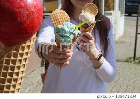Woman holding ice cream cone with colorful scoops and waffle biscuit outdoors. Sweet dessert for summer enjoyment, street food, casual lifestyle, travel moments and warm weather refreshment. Woman holding ice cream cone with colorful scoops and waffle biscuit outdoors. Sweet dessert for summer enjoyment, street food, casual lifestyle, travel moments and warm weather refreshment. 138471834