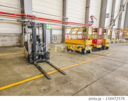 Forklift and yellow scissor lifts parked inside a large warehouse or aircraft hangar. Forklift and yellow scissor lifts parked inside a large warehouse or aircraft hangar. 138472576