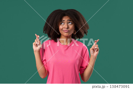 Believer African Teen Girl Praying With Crossed Fingers, Green Background. Hope Believer African Teen Girl Praying With Crossed Fingers, Green Background. Hope 138473091