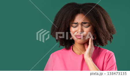 Pretty young african american girl with tooth pain on green studio background. Toothache, dental problems, dentistry and medicine concept 138473135
