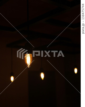 Warm glowing light bulbs hanging in a dark room Warm glowing light bulbs hanging in a dark room 138475744