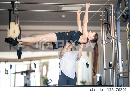 Pilates instructor assisting woman with advanced cadillac exercise 138476291