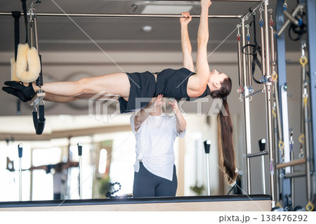 Woman practicing advanced pilates exercise with instructor assisting 138476292