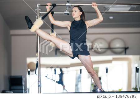 Young woman training flexibility on pilates reformer equipment Young woman training flexibility on pilates reformer equipment 138476295