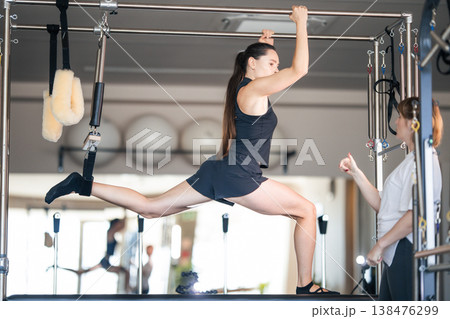 Woman practicing pilates exercise on cadillac with instructor coaching Woman practicing pilates exercise on cadillac with instructor coaching 138476299