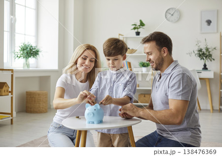 Happy smiling young family putting coins in blue piggy bank, planning family budget together. Happy smiling young family putting coins in blue piggy bank, planning family budget together. 138476369