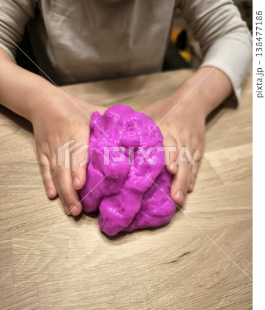 A child actively kneads and stretches a large piece of purple slime on the table A child actively kneads and stretches a large piece of purple slime on the table 138477186