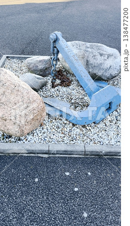 A decorative blue sea anchor against a background of light gravel and large stones A decorative blue sea anchor against a background of light gravel and large stones 138477200
