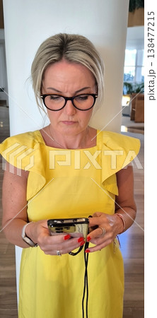 Blonde in yellow dress looks intently at smartphone Blonde in yellow dress looks intently at smartphone 138477215