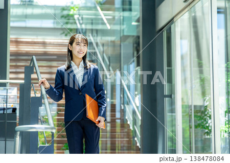 オフィスビルのエントランスを持って歩くスーツ姿の若い女性 138478084