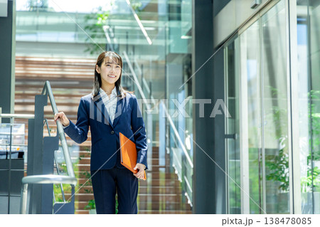 オフィスビルのエントランスを持って歩くスーツ姿の若い女性 138478085