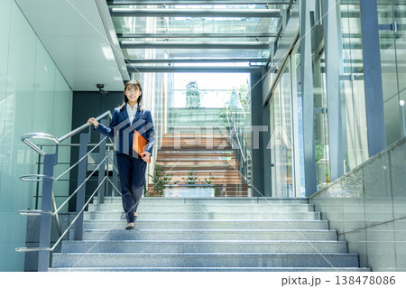 オフィスビルのエントランスを持って歩くスーツ姿の若い女性 138478086