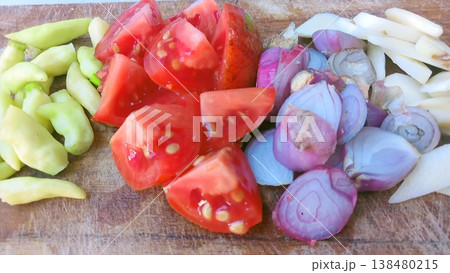 A vibrant display of fresh, chopped vegetables including red tomatoes, purple shallots, white garlic, and green chilies, neatly arranged on a rustic wooden cutting board, ready for cooking a healthy A vibrant display of fresh, chopped vegetables including red tomatoes, purple shallots, white garlic, and green chilies, neatly arranged on a rustic wooden cutting board, ready for cooking a healthy 138480215