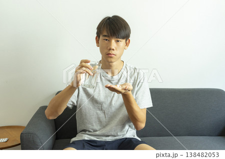 Teen boy holds a glass of water and pills. Takes medication for illness. 138482053