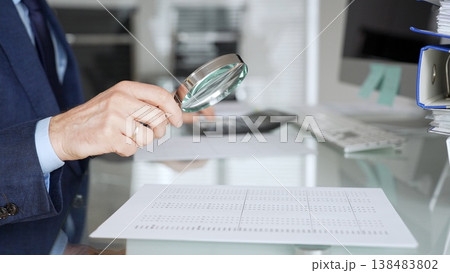 Hand holding magnifying glass, inspecting financial document, performing audit and business analysis. Audit and taxes in business Hand holding magnifying glass, inspecting financial document, performing audit and business analysis. Audit and taxes in business 138483802