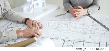 Architects collaborating, examining building blueprints with rulers and pens, developing innovative architectural designs and construction plans around a model house, close up 138483847