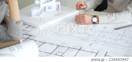 Stressed female architect analyzing blueprints and architectural model, discussing new project designs and construction plans with a colleague during a frustrating meeting, close up Stressed female architect analyzing blueprints and architectural model, discussing new project designs and construction plans with a colleague during a frustrating meeting, close up 138483947