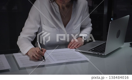 Businesswoman lawyer looking through a contract document before signing, while working in a corporate office at night. Audit, business and overworking concepts Businesswoman lawyer looking through a contract document before signing, while working in a corporate office at night. Audit, business and overworking concepts 138484016