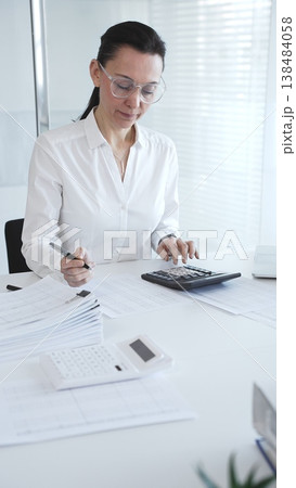 A close-up of a calculator on an office desk. A professional woman enters and analyzes financial data on a laptop, surrounded by papers and folders. Audit and taxes A close-up of a calculator on an office desk. A professional woman enters and analyzes financial data on a laptop, surrounded by papers and folders. Audit and taxes 138484058