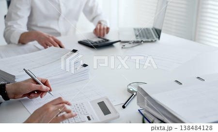 Financial professionals reviewing paperwork, using a calculator and laptop for accounting, auditing, and tax preparation. Audit and taxes theme in business Financial professionals reviewing paperwork, using a calculator and laptop for accounting, auditing, and tax preparation. Audit and taxes theme in business 138484128