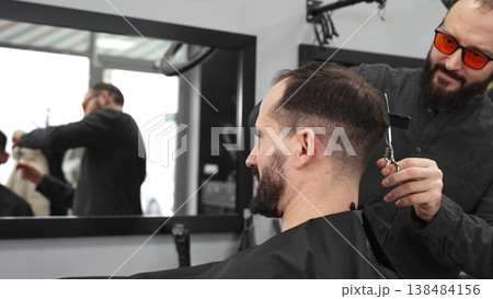 Skilled barber working on male client's hairstyle, carefully combing and preparing precision cut in contemporary barbershop setting Skilled barber working on male client's hairstyle, carefully combing and preparing precision cut in contemporary barbershop setting 138484156