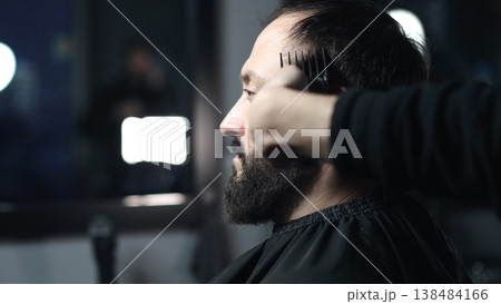 Professional barber trimming client's hair using electric clipper, creating stylish fade for bearded man in modern barbershop setting 138484166
