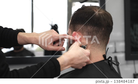 Professional barber trimming male client's hair with electric razor, delivering precise grooming service in contemporary, well lit barbershop setting 138484187