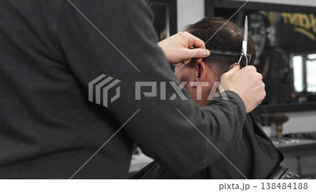 Skilled barber trimming client's hair using professional scissors, creating contemporary hairstyle in modern barbershop setting with precise, professional technique. Skilled barber trimming client's hair using professional scissors, creating contemporary hairstyle in modern barbershop setting with precise, professional technique. 138484188