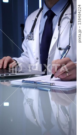 Medical professional wearing a white lab coat and stethoscope. Simultaneously typing patient data on a laptop keyboard and writing notes on a clipboard Medical professional wearing a white lab coat and stethoscope. Simultaneously typing patient data on a laptop keyboard and writing notes on a clipboard 138484224