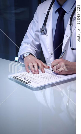 Medical professional wearing a white lab coat and stethoscope. Simultaneously typing patient data on a laptop keyboard and writing notes on a clipboard Medical professional wearing a white lab coat and stethoscope. Simultaneously typing patient data on a laptop keyboard and writing notes on a clipboard 138484225