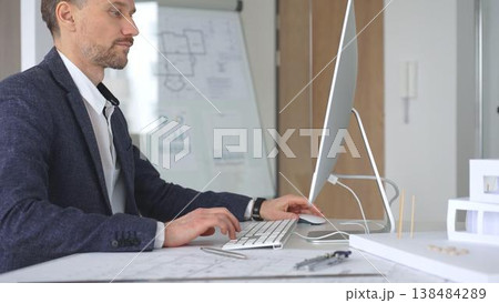 Architect designing building plans on computer, concentrating on construction project blueprints at office desk. Business and architecture concept 138484289