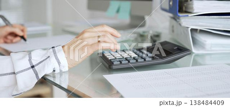 Professional woman calculating financial data using black calculator on office desk, managing expenses and budget. Audit and taxes in business Professional woman calculating financial data using black calculator on office desk, managing expenses and budget. Audit and taxes in business 138484409